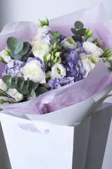 Elegant bouquet with white ranunculus, purple hydrangeas, eucalyptus leaves and lisianthus in a gift bag with lavender wrapping paper
