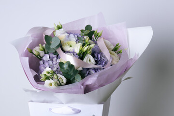 Elegant bouquet with white ranunculus, purple hydrangeas, eucalyptus leaves and lisianthus in a gift bag with lavender wrapping paper
