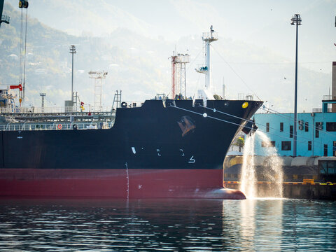 Cargo ship moored at port with ballast water discharge, maritime logistics and shipping industry.