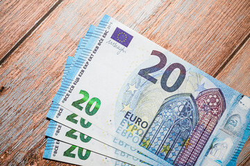Multiple twenty euro banknotes spread on rustic wooden table.