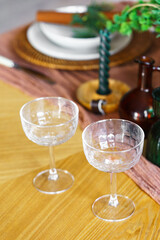 Close up of elegant crystal glasses, plates and flowers on wooden table with green decorations and warm holiday ambiance. Perfect for celebrations, cozy and romantic gatherings, seasonal home decor.