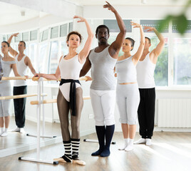Group of multiethnic male and female dancers stand in first ballet pose at barre in dance class