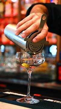 Bartender pours clear martini. A bartender pours a crystal martini through a strainer as an olive rests inside.