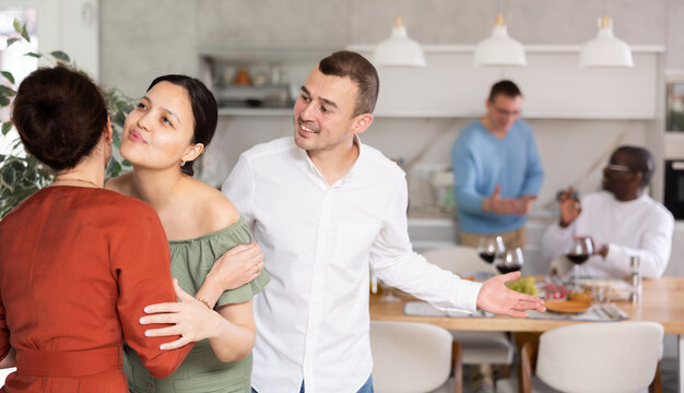 Pleased middle-aged man and woman meeting their female friend during get-together at cozy house atmosphere