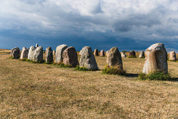 Ale stones monument standing in the golden field under a cloudy sky, representing a ship setting and offering a glimpse into ancient Nordic history and heritage