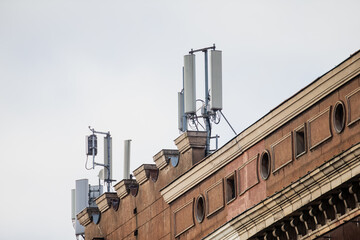 Rooftop cellular equipment mounted on historic facade with several communication panels, wiring and support frames visible under cloudy sky in urban environment