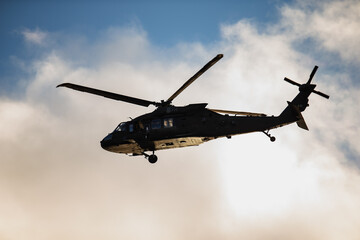 Armed forces helicopter showing tactical fuselage, dual rotor system and underbelly equipment in clear airborne movement against illuminated sky