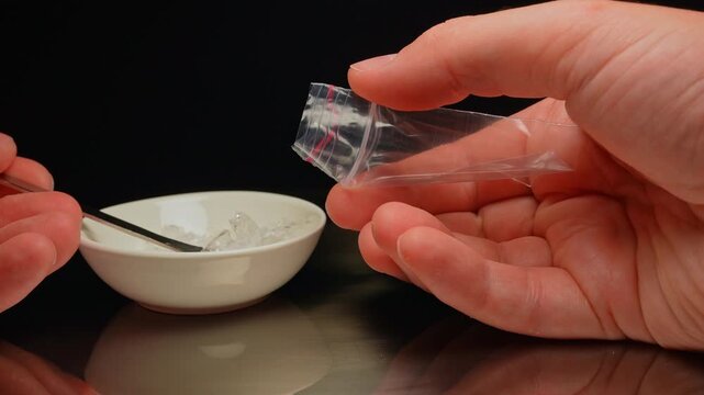 Drug dealer preparing and packaging Fentanyl Crystal meth or Crack Cocaine for sale and distribution. Drug trafficking and addiction crises. Crystals use in glass tube or stems and primarily smoking.