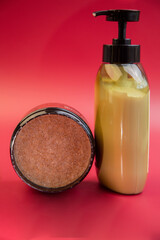 Skincare essentials include a brown sugar scrub in a round container and a creamy lotion in a pump bottle, set against a bright red backdrop, emphasizing beauty routine