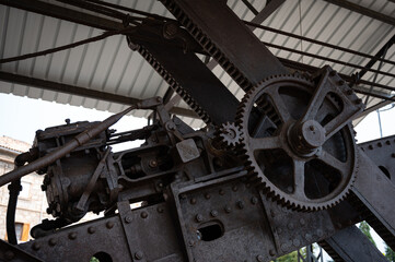 Detail of the massive, rusty drive mechanism on the boom of the steam shovel, showing the power transfer gear and chain linkage.
