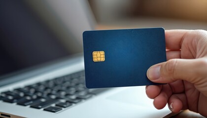 Hand holding a blue credit card near a laptop keyboard. Online shopping digital payment concept. Fintech e-commerce theme. Modern tech finance business.