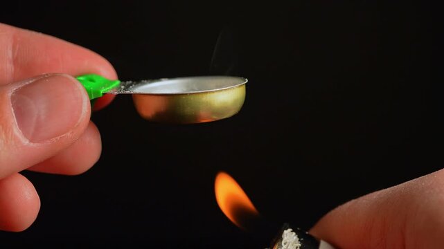 Drug user preparing liquid drugs in the tin cooker container used for mixing and heating a drug with lighter. Drug such as cocaine, white heroin or crack cocaine mixed and dissolved with water.