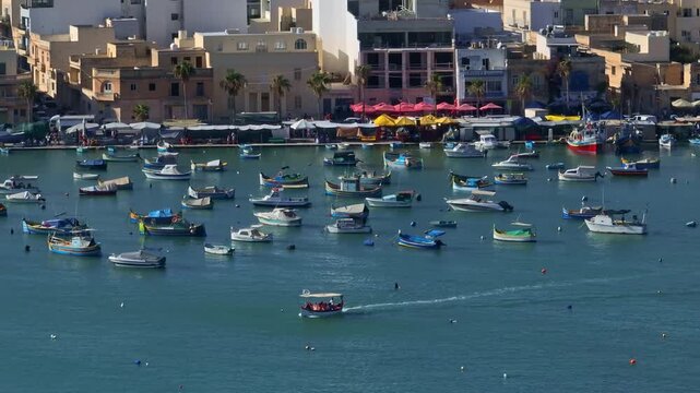 Malta, Marsaxlokk Harbour: Traditional Maltese luzzu boats creating a vibrant display in Marsaxlokk harbor, while a tourist boat navigates the picturesque Mediterranean scene