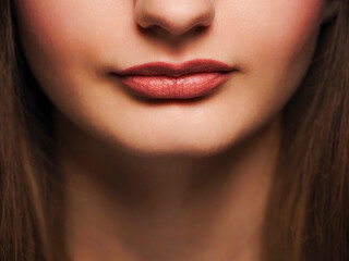 Fototapeta premium Lips with red lipstick on a face of beautiful young female model. Beauty and fashion industry. Showcasing cosmetic products.