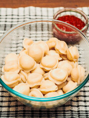 Fine portion of traditional Russian dumplings in a glass bowl, red souse in small glass bowl. Fine dinner with simple food.