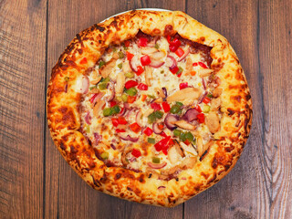 A cooked pizza with a lot of toppings including chicken, peppers, and onions. The pizza is sitting on a wooden table. Fine Italian style meal popular world wide. Rich dough base.