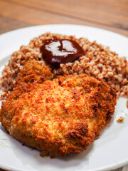 Simple buckwheat meal with breaded chicken fillet on white plate on wooden table. Tasty and healthy food.