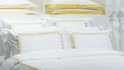 A bed with a white comforter and gold stripes. There are four pillows on the bed