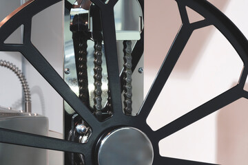 A black wheel with a chain on it. The chain is attached to a metal rod, industrial concept background