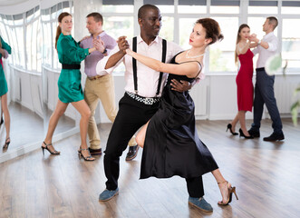 Fototapeta premium Pair of woman and African American man enjoying of sensual tango dance in choreo class. Exciting hobby, active lifestyle, passion for dancing and choreography