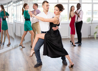 Dynamic young male and female attendees of dancing courses doing waltz in group