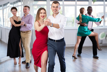 Positive young man and woman practicing waltz in pair in dancing studio