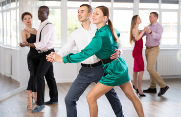 Fototapeta premium Dynamic young male and female attendees of dancing courses doing waltz in group