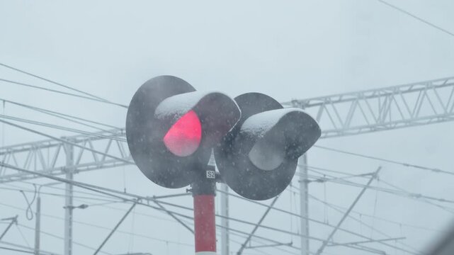 Red train signal surrounded by snow with blurred tracks in winter weather