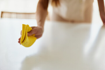 Hand holding yellow cloth cleaning and wiping white table surface, woman performing household chore, closeup of wipe motion and detail for domestic cleaning and surface care at home.