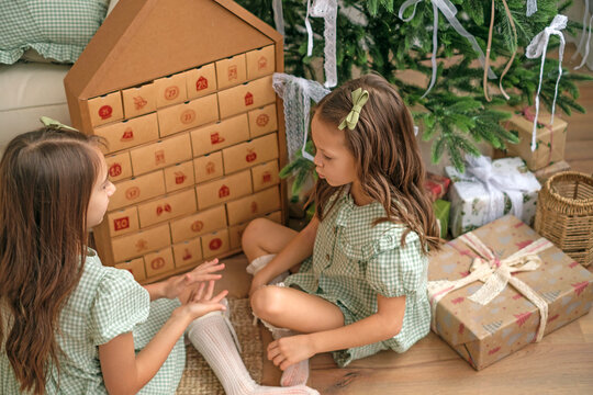 Children are sitting at the Christmas tree next to the Advent calendar, curious and eager to open the cell of the new calendar day. The approach of the new year