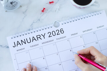 January 2026 calendar with coffee cup, alarm clock and hand holding a pen. New year planning,...