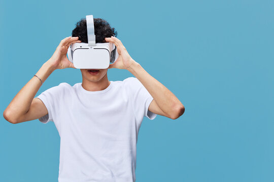 young man wearing virtual reality headset explores digital environment, immersive technology experience, casual white t-shirt, blue background