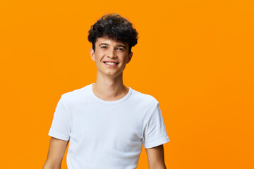 young man smiling brightly in white t-shirt, casual style with curly dark hair, vibrant orange background, positive and energetic mood