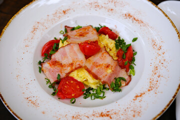 Fried eggs with bacon decorated with tomato and green onion on a wooden board. High quality photo
