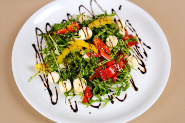 Caprese salad with arugula, mozzarella, cherry tomatoes, fresh basil and balsamic glaze on a white plate on a gray concrete background. Top view, copy space. High quality photo