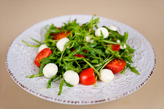Fresh green salad made with mozzarella cheese, cherry tomatoes, arugula and olive oil on white stone table background. Healthy food and diet concept. Flat lay, copy space. High quality photo