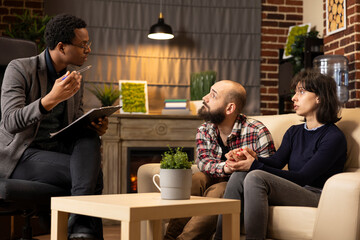 Black male therapist provides psychological guidance, helping couple navigate family crisis and relationship challenges. Private clinic session emphasizes marriage counseling and mental wellbeing.