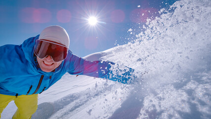 LENS FLARE, CLOSE UP: Smiling snowboarder enjoys riding fresh snow on untracked slope, hand buried...