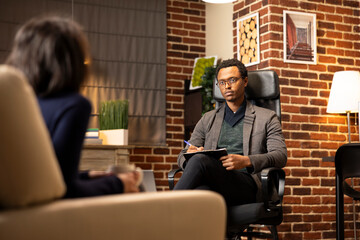 African American counselor wearing glasses listens attentively to young couple. Professional counseling session supporting patients with depression, stress and emotional challenges.