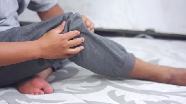 A young man massages his knee due to knee pain and muscle aches caused by Runner's Knee or Patellofemoral Pain Syndrome, osteoarthritis, arthritis, rheumatism, and Patellar Tendinitis. Medical concept