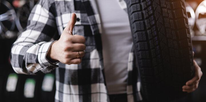 Young caucasian male holding car tire and giving thumbs up in auto shop, banner tyre store