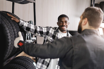 African male customer discussing tires with caucasian male mechanic in auto shop