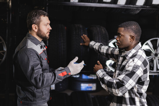 Male mechanics and african men discussing winter tire options in auto shop setting