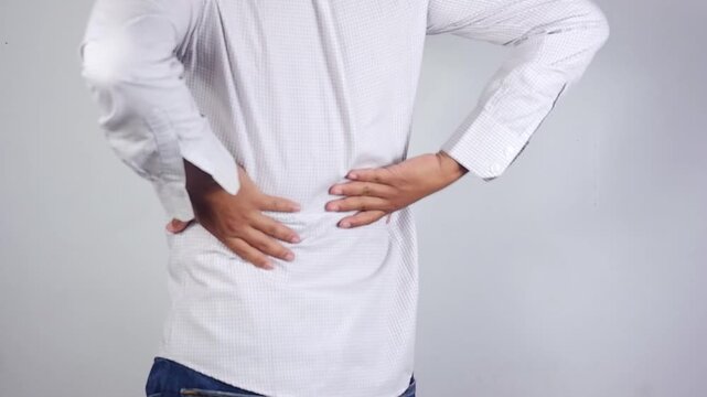 Lower back pain, young man experiencing lower back pain after working from home. An adult man holding and massaging his lower back, chronic back pain, bone calcification, osteoporosis. Healthcare conc