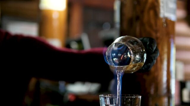 The bartender sets fire to the sambuca in a beautiful wine glass and pours it into another. preparing cocktails at the bar. High quality 4k footage