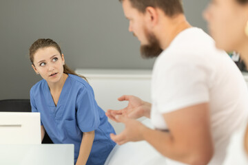 Obraz premium Man stands near the reception of a dental clinic and asks the administrator questions about making an appointment with a doctor. Couple came to the dentistry studio for appointment
