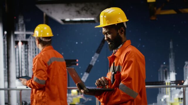 Black offshore workers conduct risk assessment on oil platform at sea, using modern technology and laptop to improve drilling rig safety. Fossil fuels and natural gas extraction. Camera B.