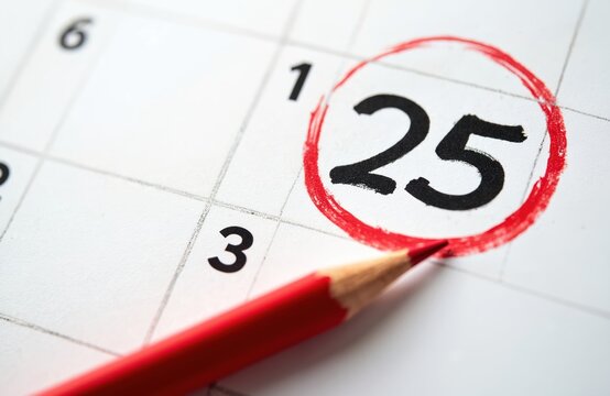 Close up photo shows calendar page with day 25 circled with red pencil. Focus is on date mark with a red pencil on a white background. Event reminder date concept.