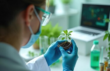 Female scientist studies small plant sample in lab. She wears protective gear while working. A laptop and beakers are in the background reflecting modern scientific research.