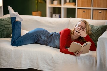 Obraz premium Woman yawning while reading book on sofa